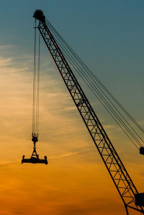 Free A tower crane silhouette set against a vibrant orange sunset sky in Reykjavík, Iceland. Stock Photo