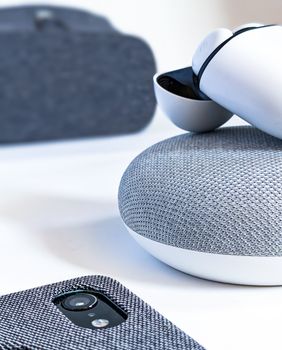 Close-up of wireless earbuds, smartphone, and smart speaker illustrating contemporary tech design.