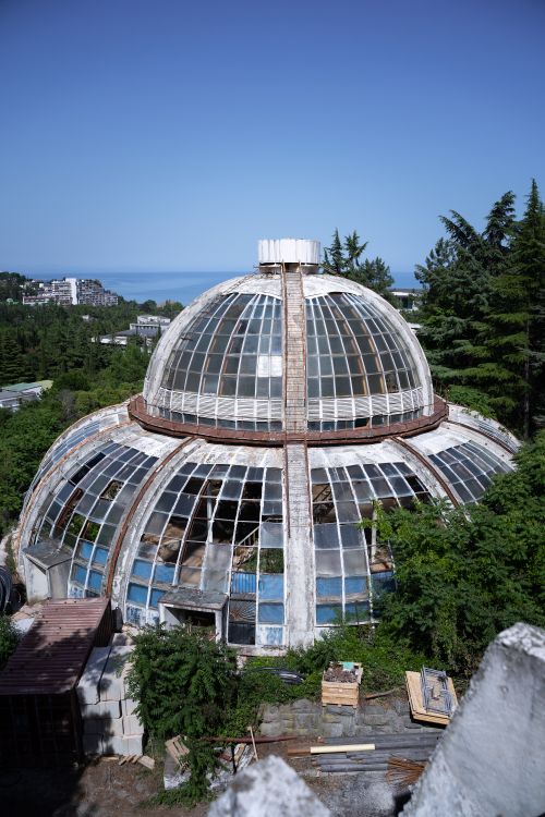 Free A striking abandoned glass dome greenhouse surrounded by lush greenery against a clear sky. Stock Photo