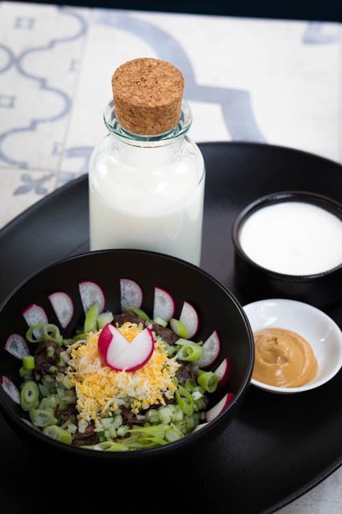 Free 牛奶瓶旁邊的蔬菜沙拉和棕色醬浸在圓形黑色托盤上 Stock Photo