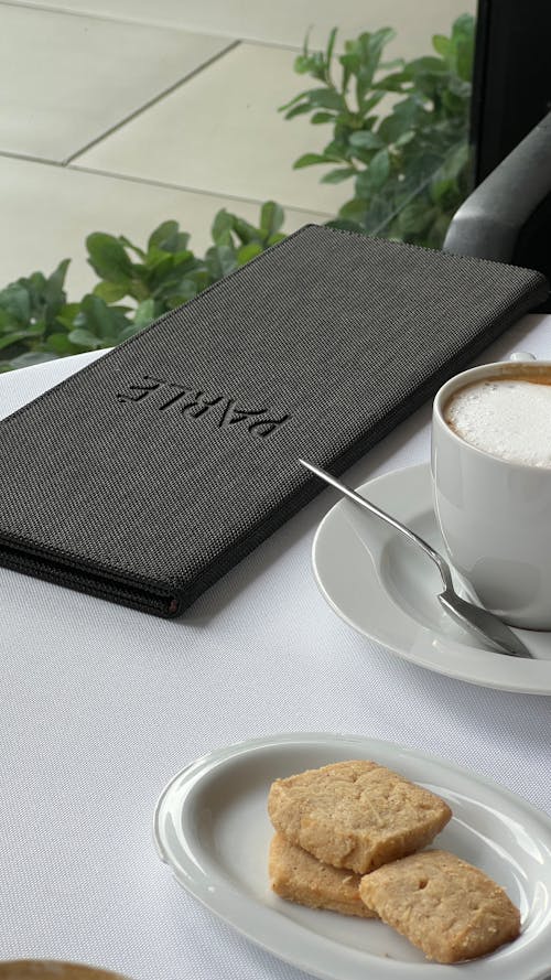 Photo of a Cup of Coffee, Biscuits on a Plate and a Black Case