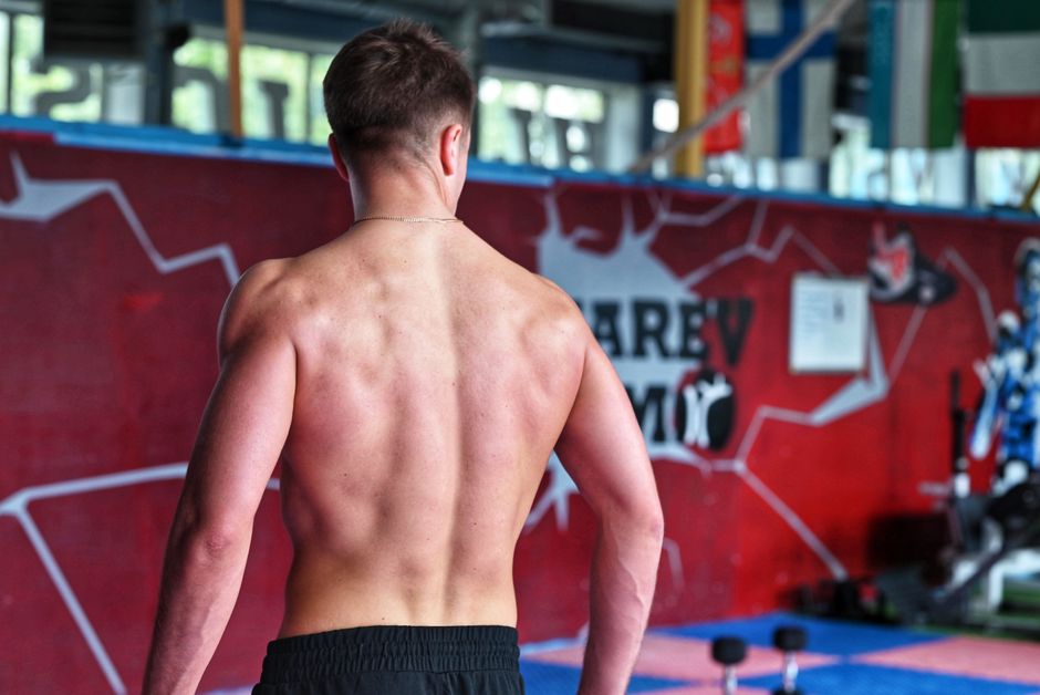 Shirtless man showcasing muscular back indoors in fitness gym.