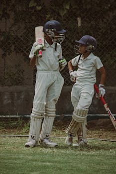 Two young cricketers in full gear discussing strategy on the field in Gahunje, India.