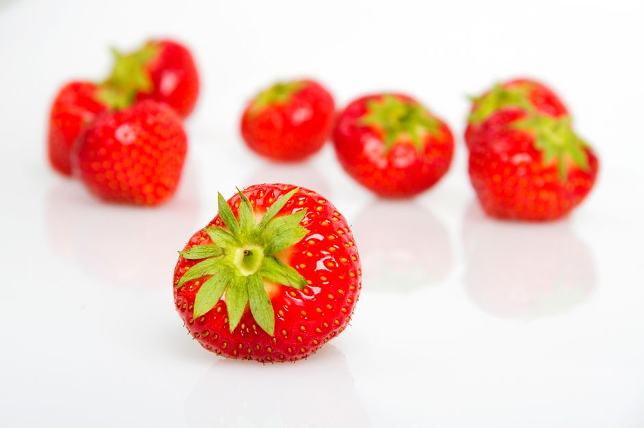 Close-up of juicy, fresh strawberries with green tops on a clean white surface.