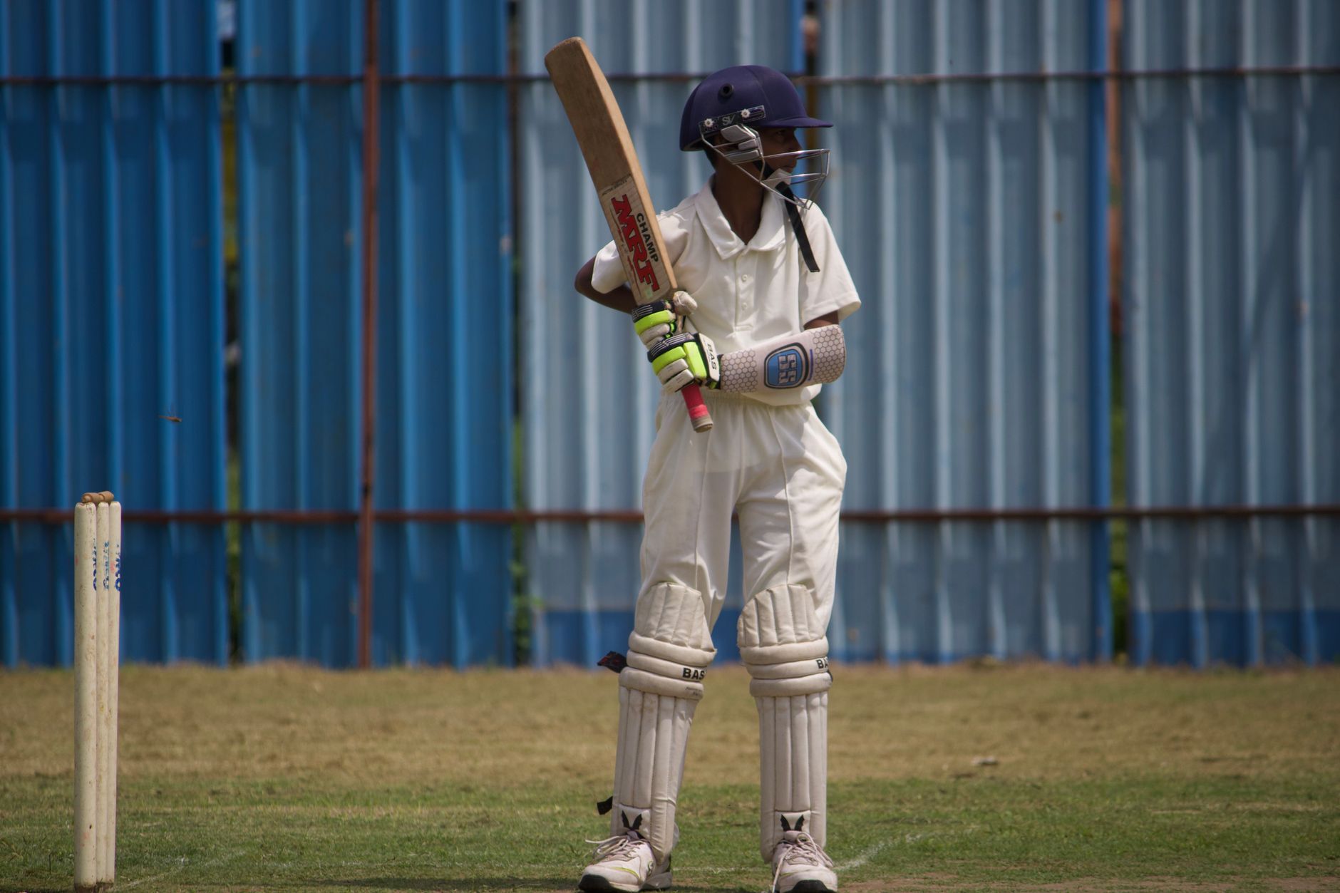 Youth cricket player in protective gear poised to bat during a sunny day on the field.