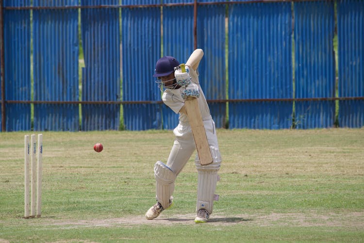 A Man Playing Cricket On The Grass Field