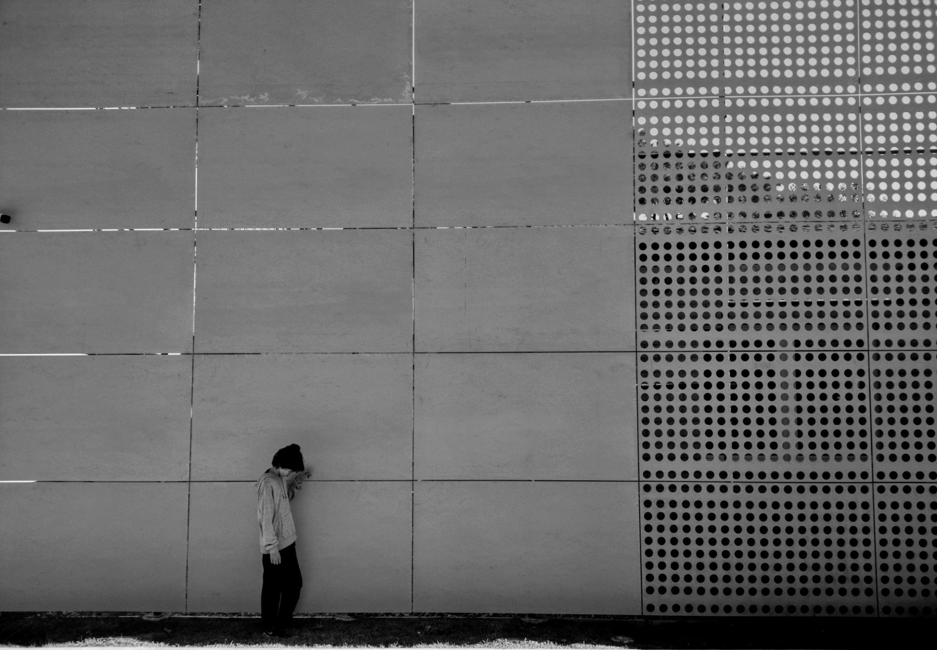 A person stands against a modern perforated wall in an urban setting, creating a minimalist aesthetic.