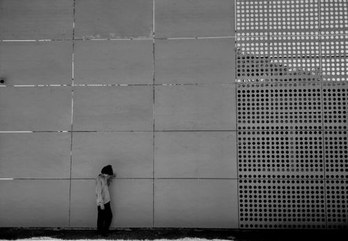 Free A person stands against a modern perforated wall in an urban setting, creating a minimalist aesthetic. Stock Photo