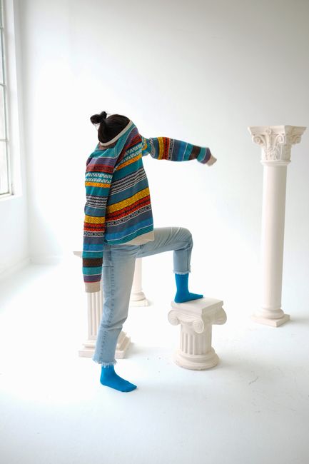 A model poses creatively with columns, wearing a colorful sweater and jeans in a studio.