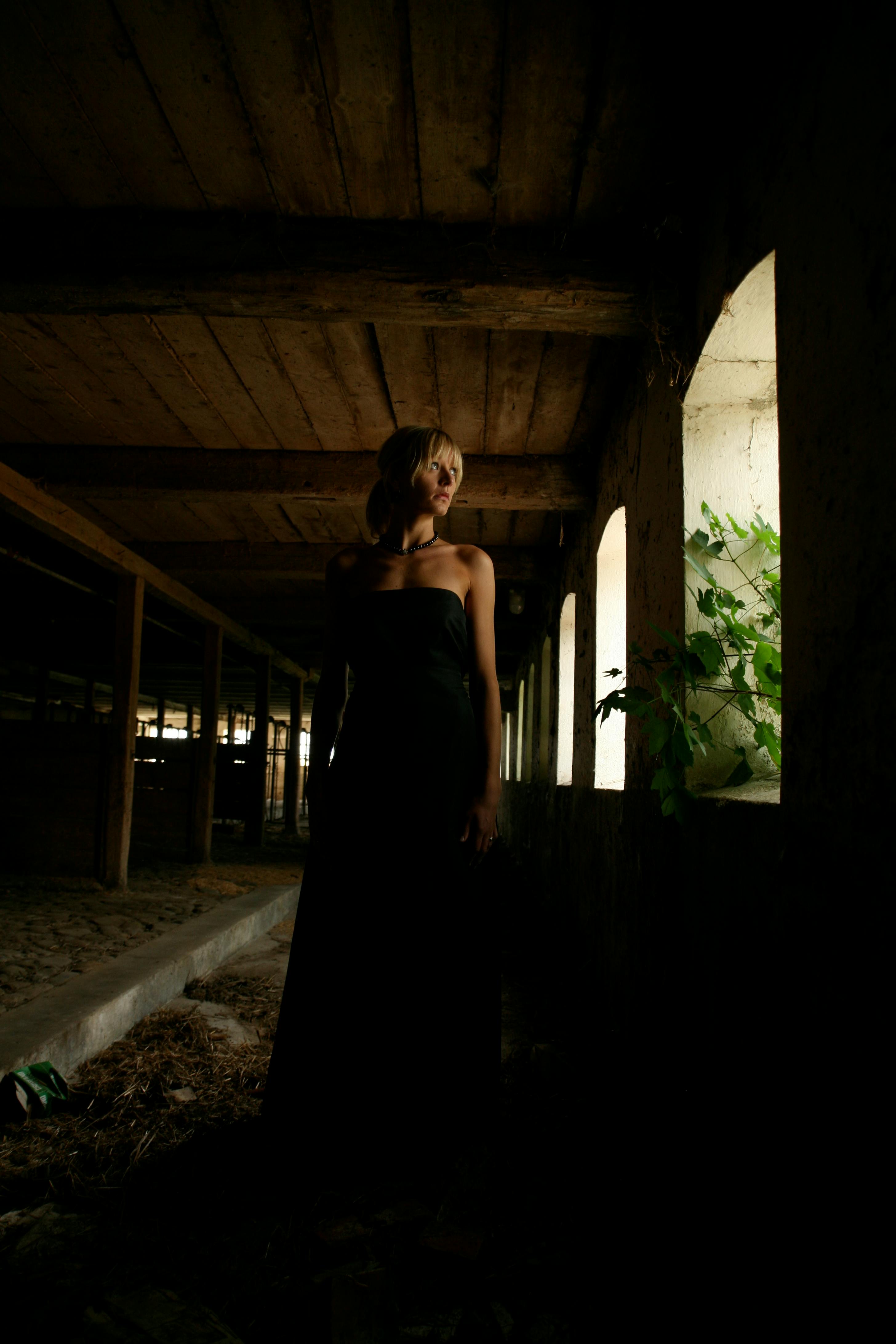 一名女子身穿深色连衣裙，在一栋怪异的废弃建筑中优雅地摆出姿势