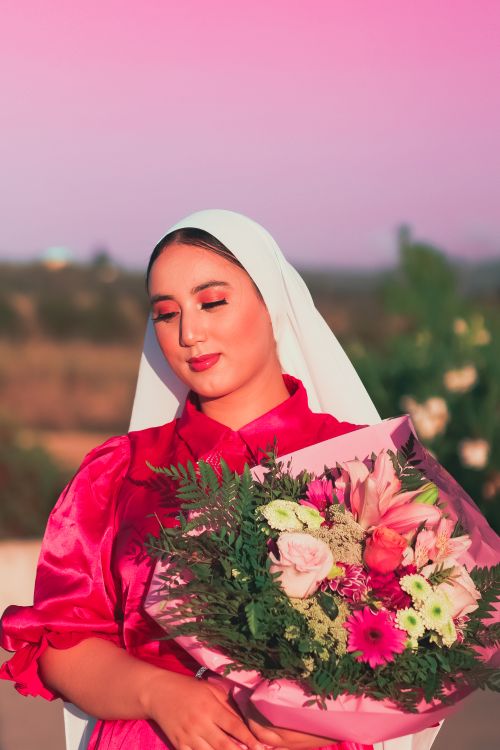 Free A woman in traditional attire holds a vibrant flower bouquet against a sunset backdrop. Stock Photo