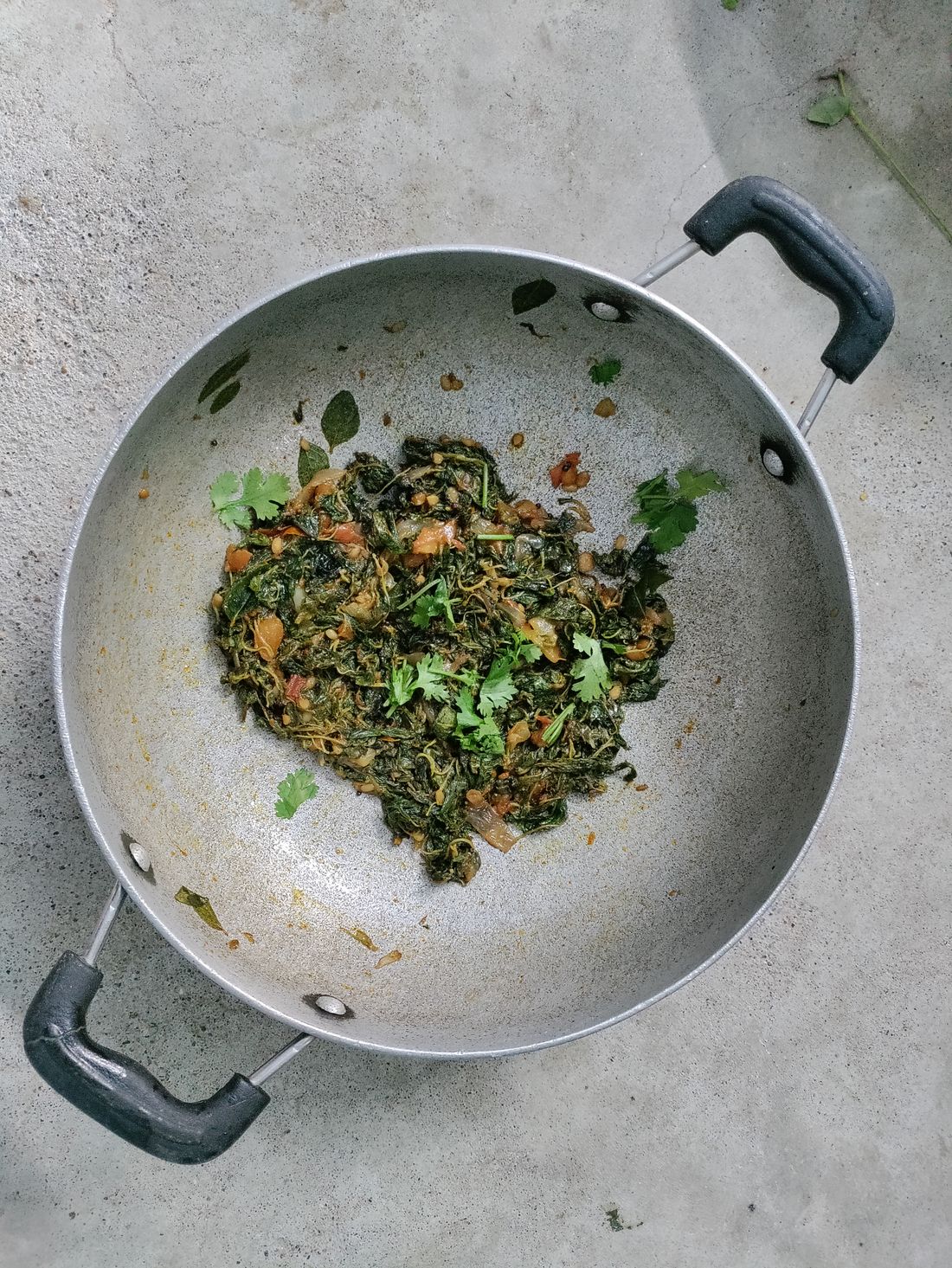 Stainless steel kadhai with sautéed greens, seen from above