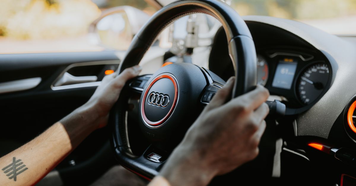 A close-up view of hands gripping a car steering wheel with dashboard visible.