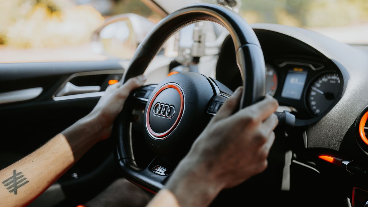 A close-up view of hands gripping a car steering wheel with dashboard visible.