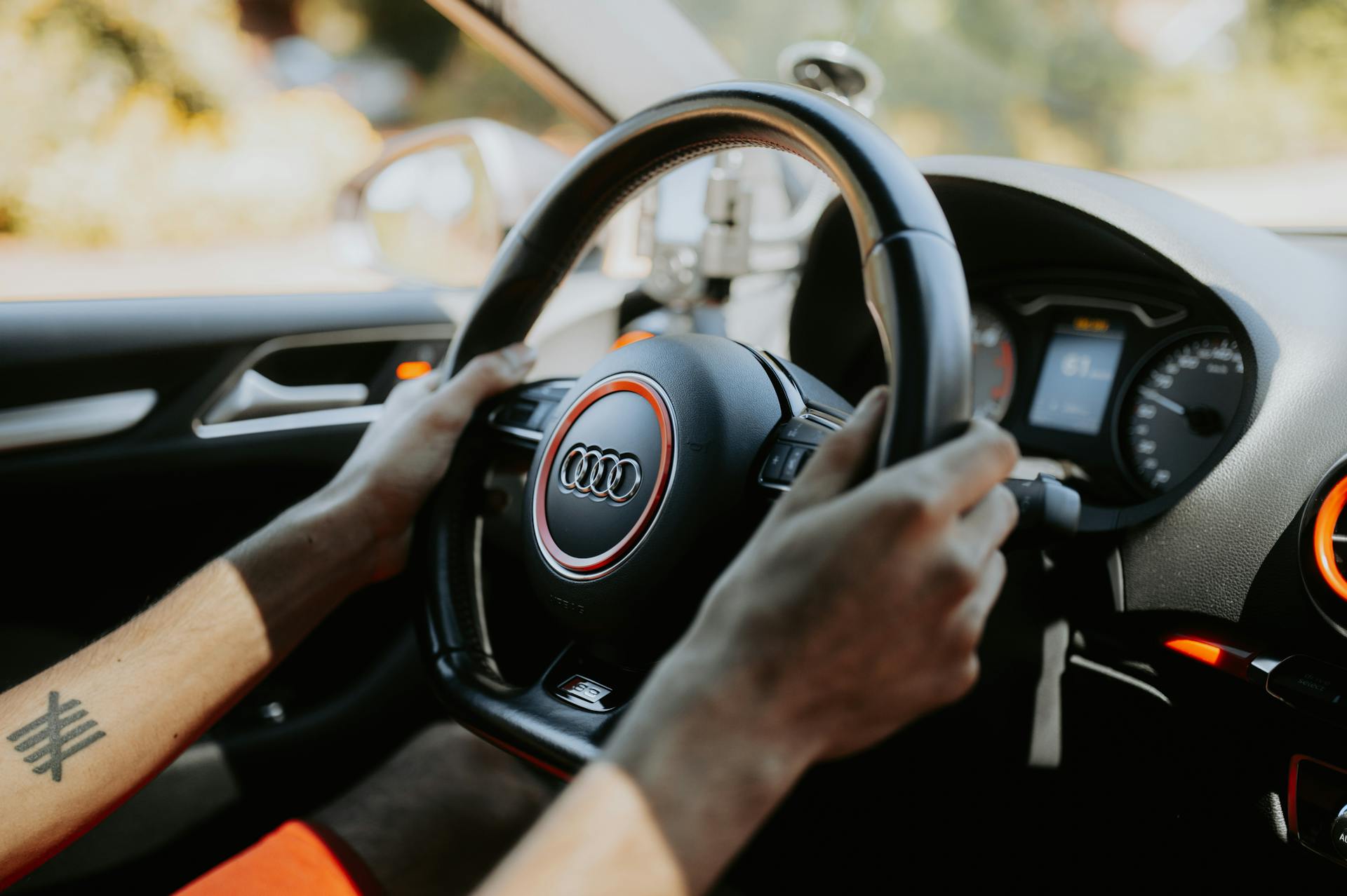 A close-up view of hands gripping a car steering wheel with dashboard visible.