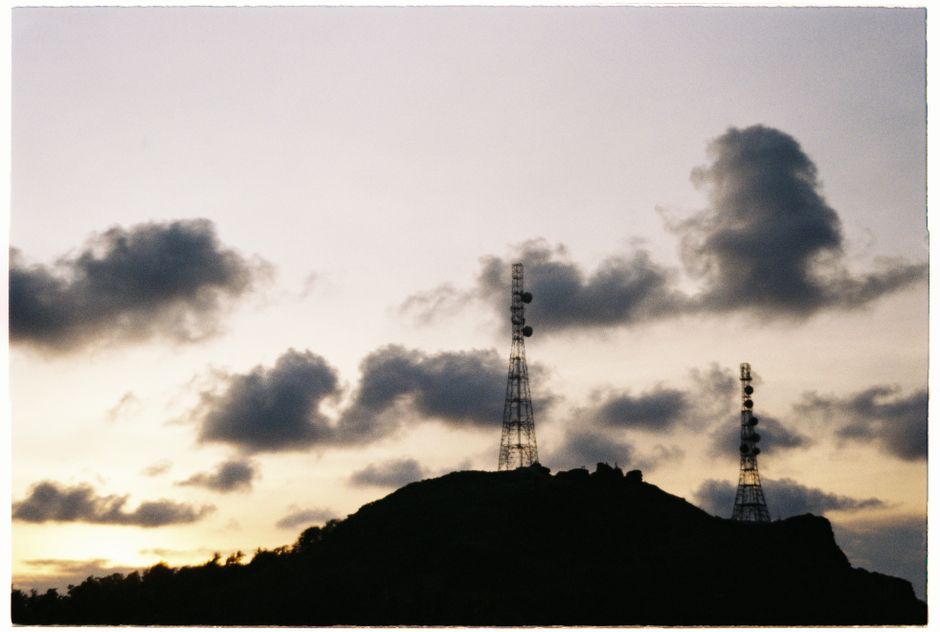 Silhouetted transmission towers against a vibrant cloudy sunrise sky on a hillside.