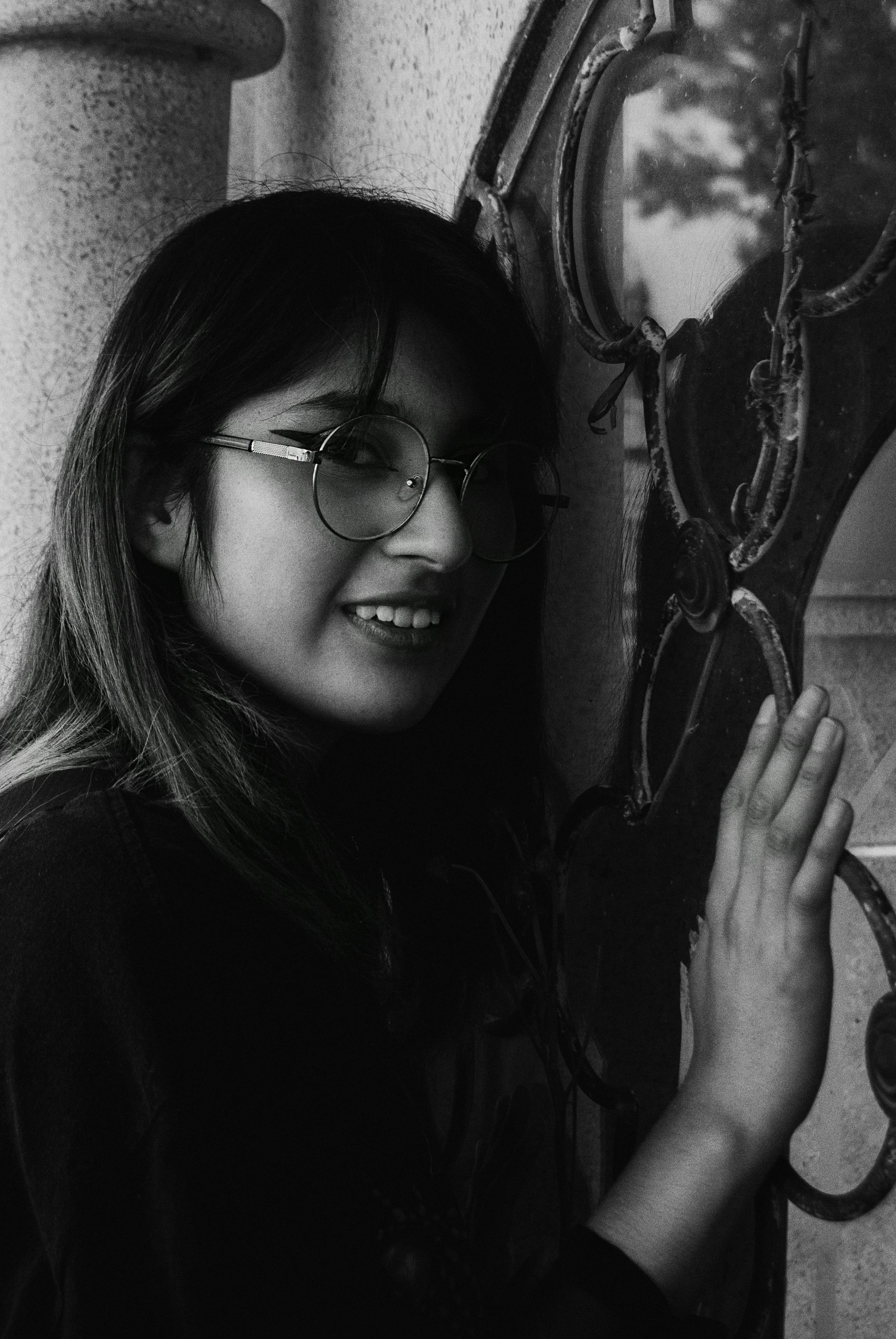 Elegant black and white portrait of a smiling woman with glasses posing by a decorative gate.