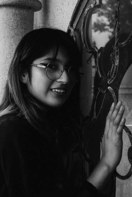 Free Elegant black and white portrait of a smiling woman with glasses posing by a decorative gate. Stock Photo