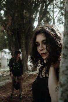 Two women in gothic attire in a moody forest setting, exuding mystery and fashion.