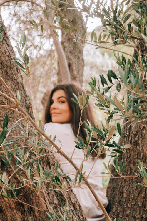 Woman in White Shirt is Sitting in Between Tree Trunks