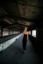 一名身穿黑色连衣裙的妇女，走过一条光线昏暗的废弃工业走廊