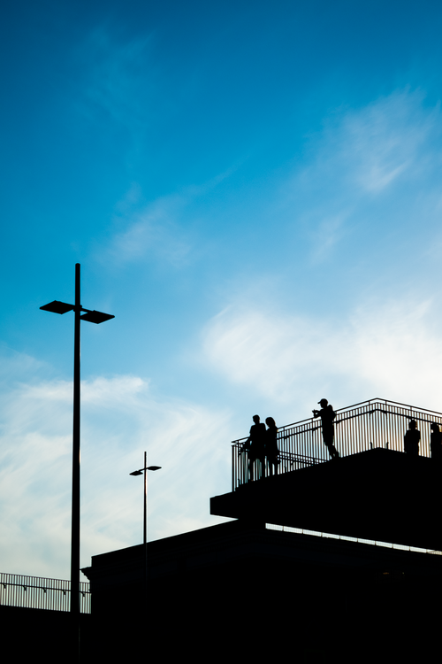 Free Silhouetted figures on a rooftop against a blue sky create a dramatic cityscape scene. Stock Photo