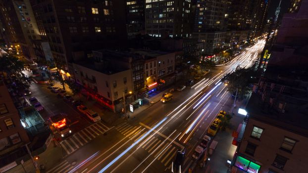 Aerial view of busy New York City street at night with vibrant light trails and cityscape.