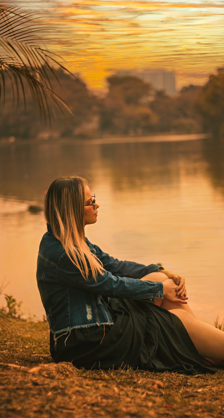 Woman Sitting On River Bank On Sunset