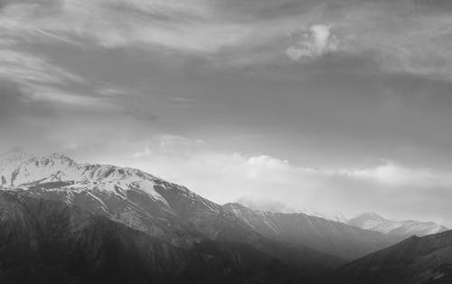 Grayscale Photo of Mountains Under Cloudy Sky