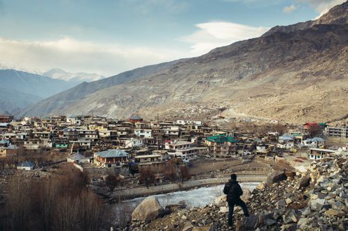 Free A lone traveler overlooks a picturesque mountain town in India, surrounded by rugged terrain and serene landscape. Stock Photo