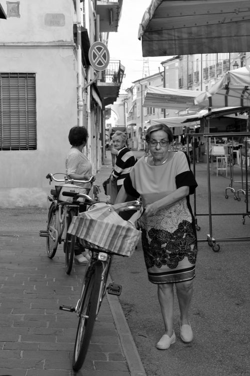 Free Monochrome scene of an elderly woman with a bicycle in a bustling street market in Revere, Italy. Stock Photo