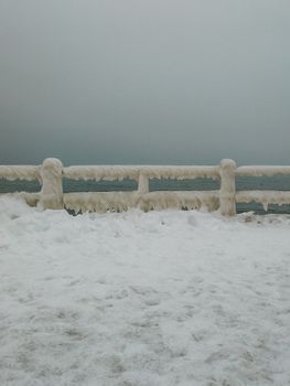 Enveloped in winter's embrace, frozen railings along Constanța seafront in Romania showcase a serene icy landscape.