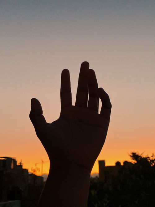 Free A silhouetted hand reaches towards a colorful sunset sky, capturing a moment of tranquility and awe. Stock Photo