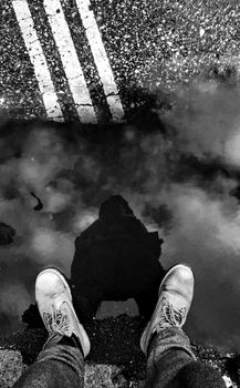 Monochrome image showing shoe reflection in a puddle on a street, capturing urban mood.