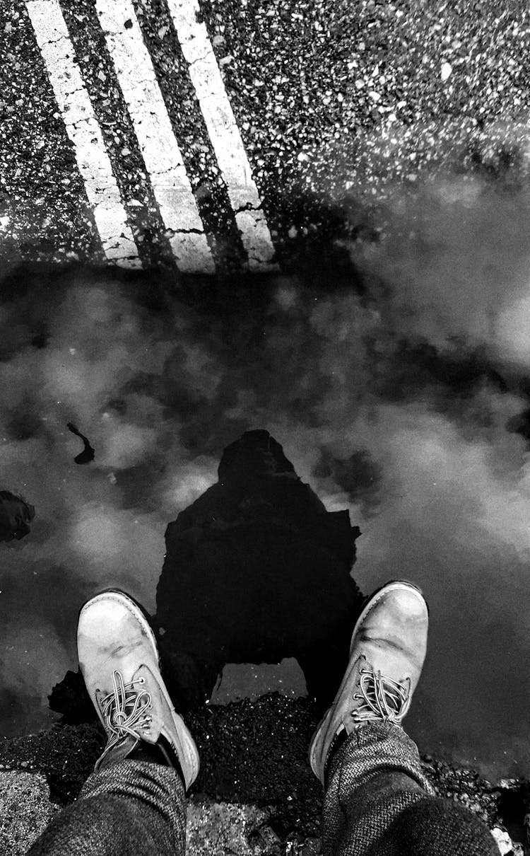 A Person In White Sneakers Standing On Road With Water