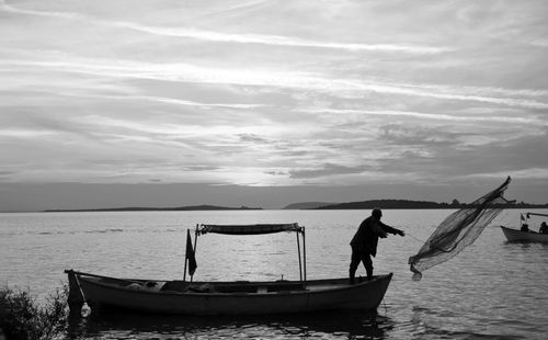 Free Black and white image of a fisherman casting a net from a boat at sunset over the ocean. Stock Photo