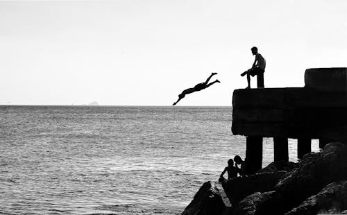 Free Silhouettes of People Jumping from Pier into Water Stock Photo