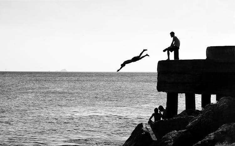 Silhouettes Of People Jumping From Pier Into Water