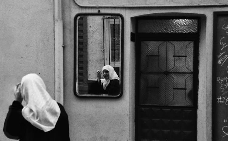 Old Woman In Handkerchief On Head Looking In Mirror