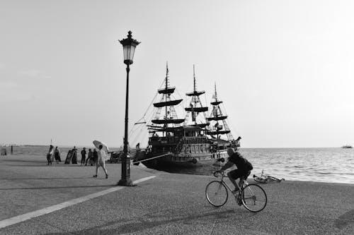 Grayscale Photo of a Person Riding a Bicycle near Body of Water
