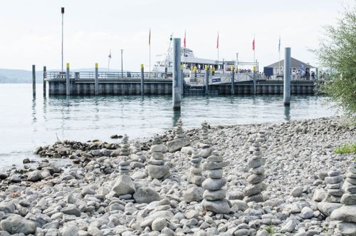 Free Calm lake view with stacked rocks and a docked ship in the background. Stock Photo