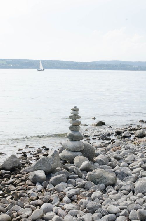 Free A serene coastal scene with stacked stones and a distant sailboat. Stock Photo
