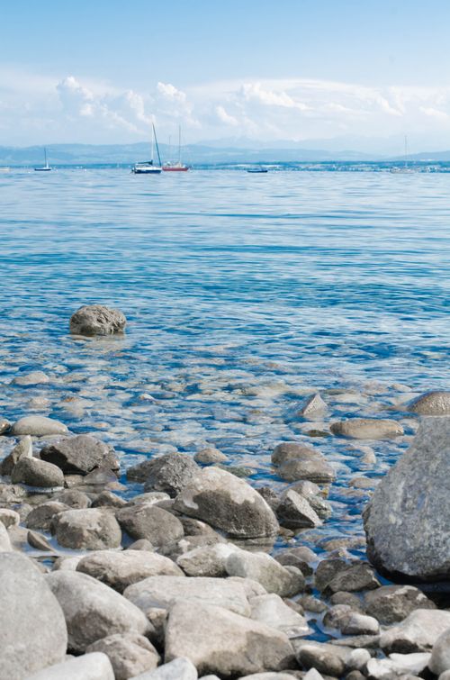Free Peaceful beach scene with rocks and sailboats on the horizon under a clear blue sky. Stock Photo