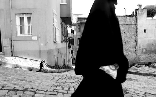 Free A black and white street scene with a woman in a veil and a cat on a cobblestone road. Stock Photo