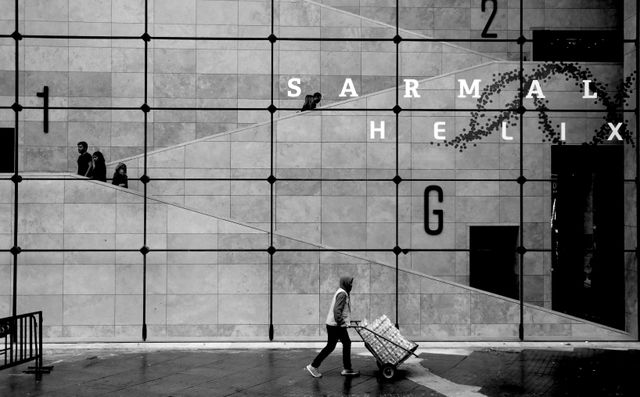 Black and white image of a modern building with people and unique wall design.