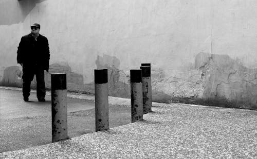 Grayscale Photography of Man Walking Beside the Concrete Wall