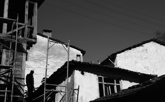 Black and white photo of a man on scaffolding among old buildings.