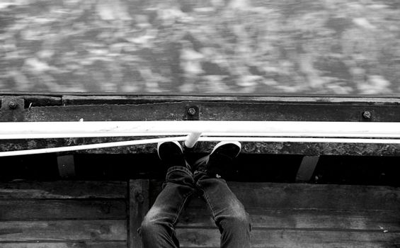 Black and white image of legs hanging over a boat's edge, showing motion blur of water.