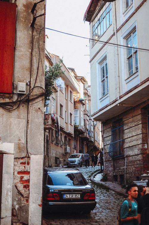Free Picturesque narrow street featuring old buildings, parked cars, and pedestrians. Stock Photo