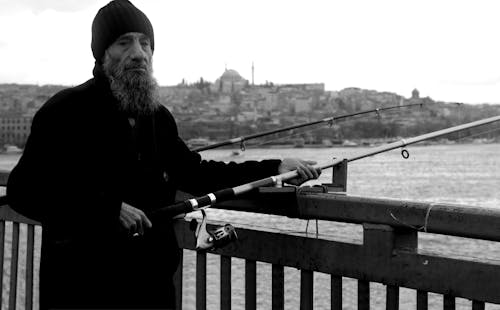 Grayscale Photo of Man in Black Jacket Holding Fishing Rod